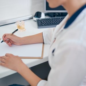 Woman in medical uniform writing at desk