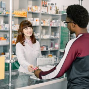 Young woman pharmacist giving medications to the male African client standing at the paydesk of the